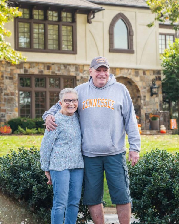 A man and woman standing together in front of their house after getting a new roof from Barnett Roofing