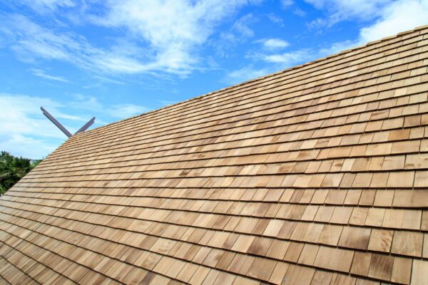 Wooden shingle roof on a building under a bright blue sky with scattered clouds, showcasing quality residential roofing by Barnett Roofing.