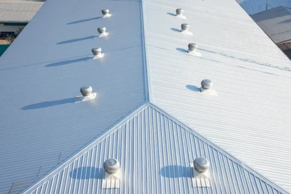 Aerial view of a large corrugated metal commercial roofing with multiple evenly-spaced turbine vents casting long shadows.