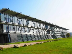 Modern glass and steel office building with angled windows, featuring premium metal roofing by Barnett Roofing, set on a grassy lawn with rocks and a clear blue sky in the background.